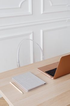 Modern minimalist workspace featuring a laptop and notebook on a wooden desk with white walled background.