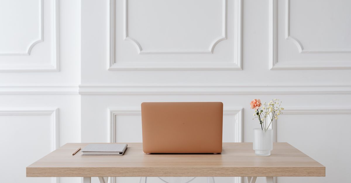A serene workspace featuring a simple desk with a laptop, notebook, and a vase of flowers.