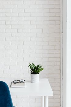 A modern office setup featuring eyeglasses and a plant on a desk against a white brick wall.