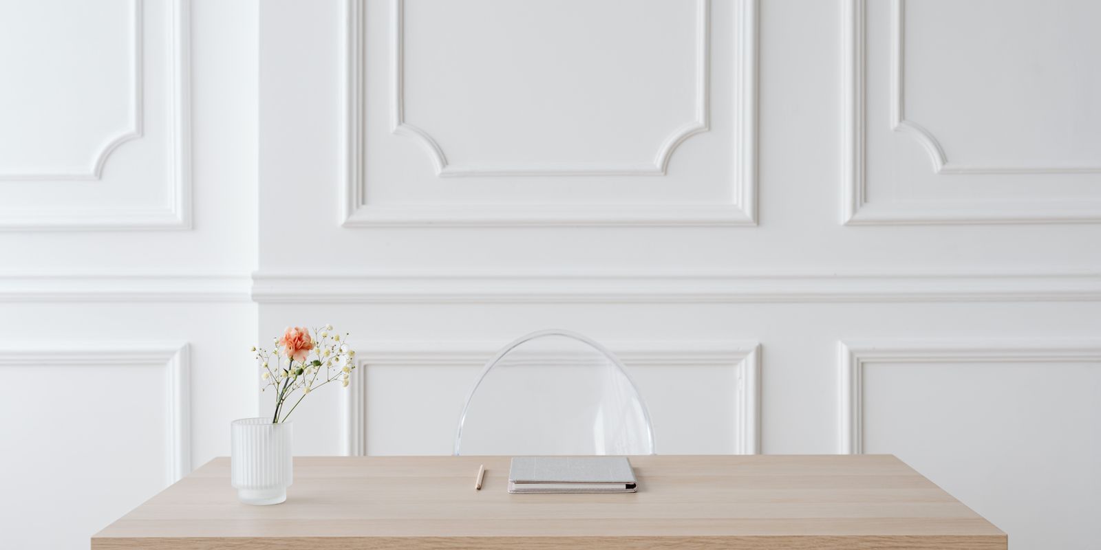 A minimalist white desk with a small flower vase, chair, and phone, surrounded by empty space