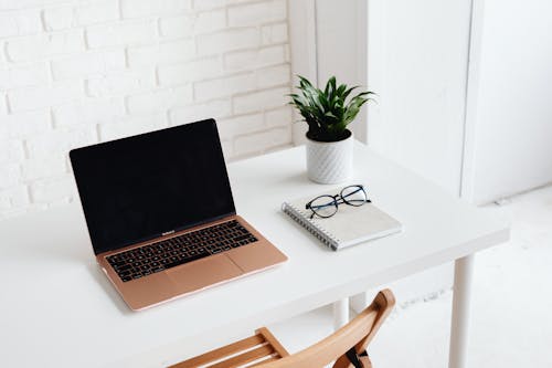 Free Laptop on White Table With Notebook and Eyeglasses Stock Photo