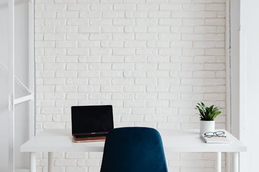 Modern home office featuring a laptop on a white desk against a sleek white brick wall.