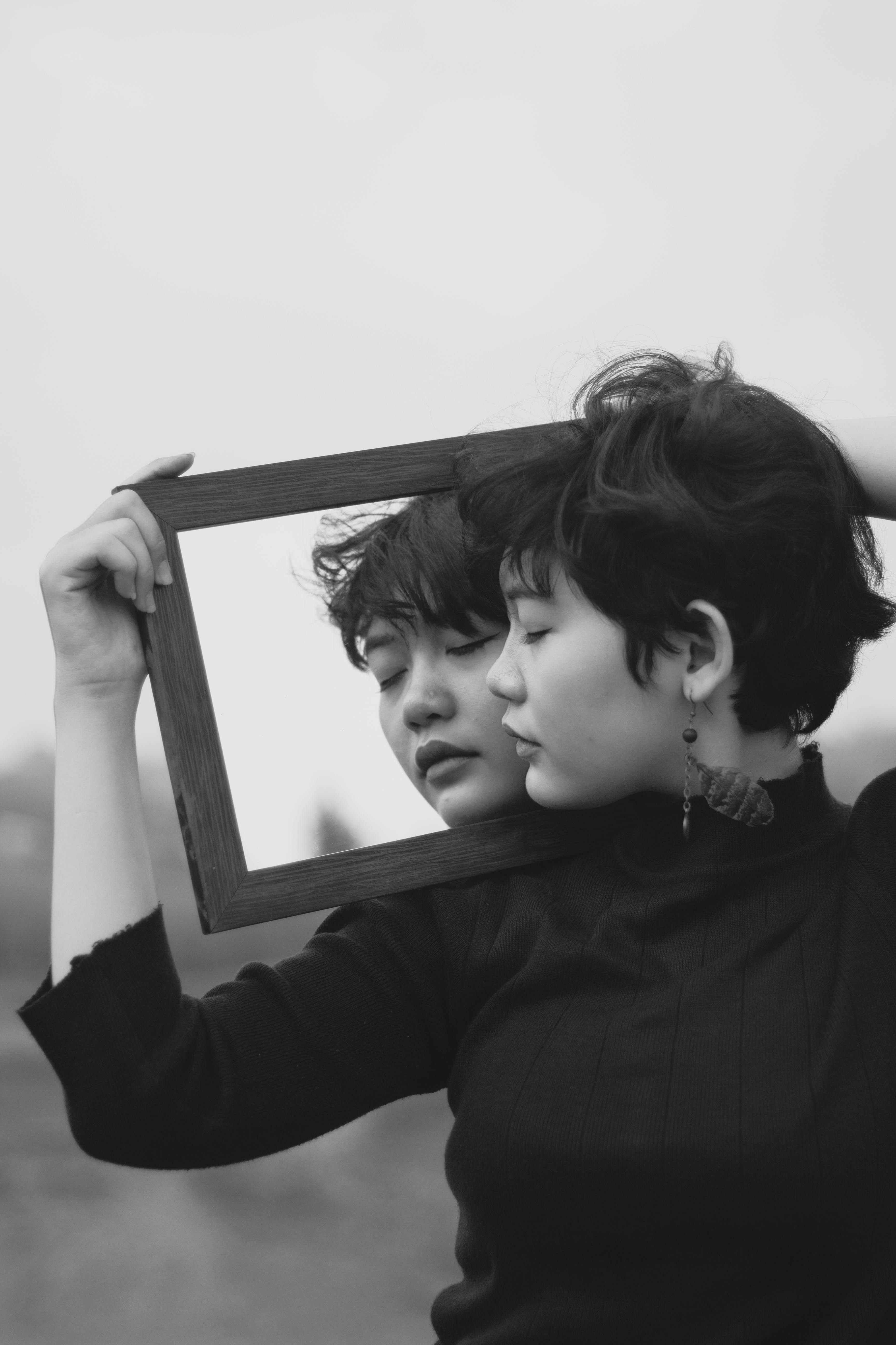 A thoughtful monochrome portrait of a woman with a mirror reflection outdoors.