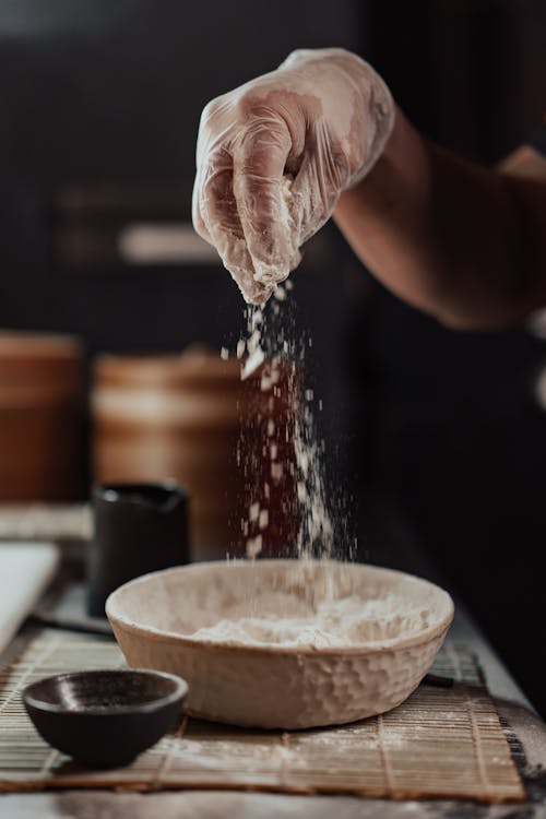Free Person Sprinkling Flour Above White Ceramic Bowl Stock Photo