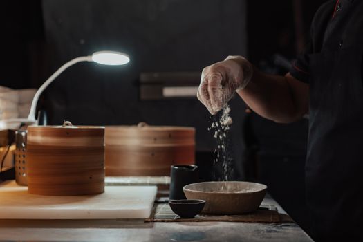 Chef sprinkles flour while preparing dumplings in a cozy kitchen setting with bamboo steamers.