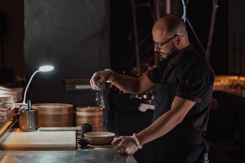 Man in Black Chef Uniform Sprinkling Flour on Ceramic Bowl