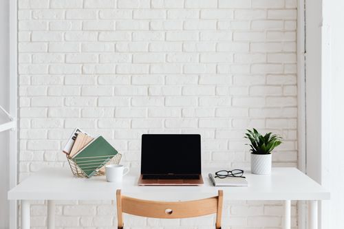 Free Clean and organized white workspace with laptop, plant, and books against a brick wall. Stock Photo