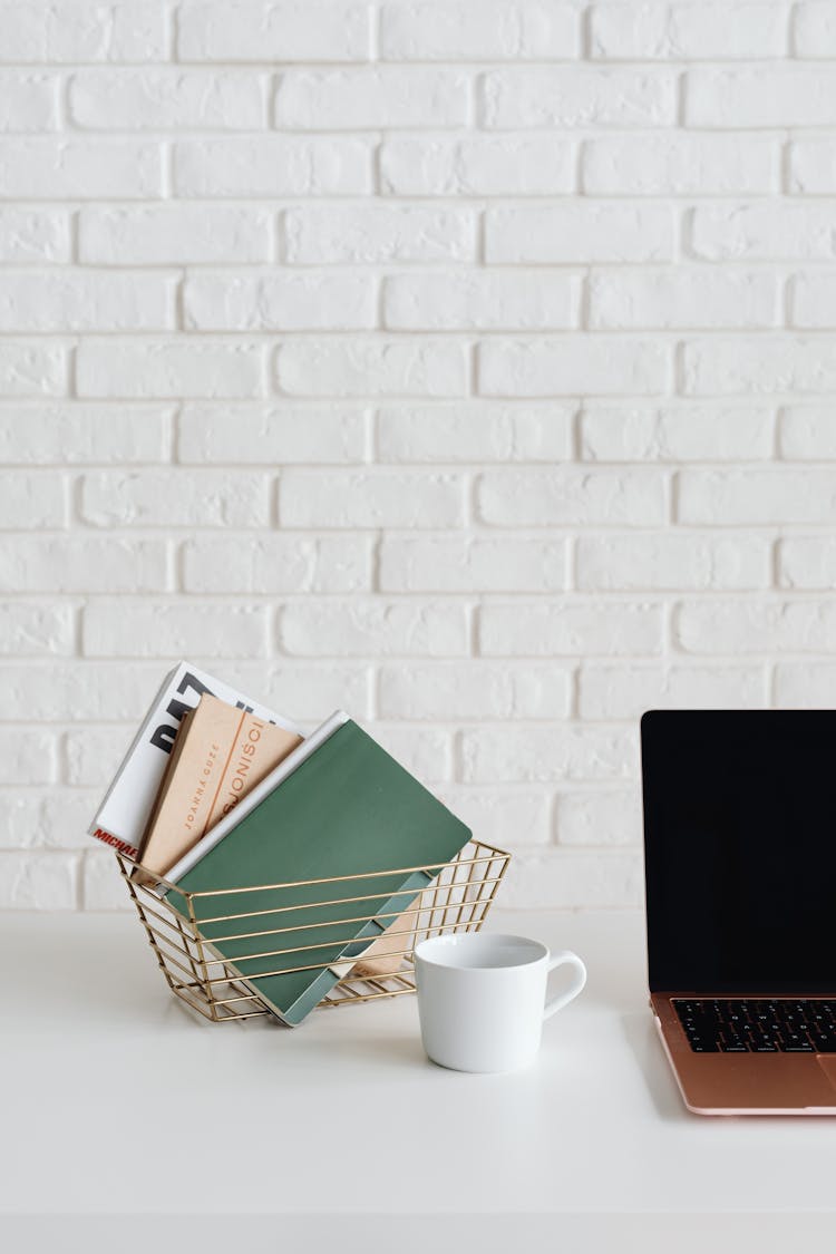 Notepads In Metal Basket On White Table Beside Laptop