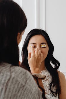 A young woman with creative floral eyelid makeup using daisies, in an elegant indoor setting.