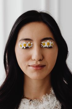 Elegant portrait of a woman with daisies on closed eyes, symbolizing nature and beauty.