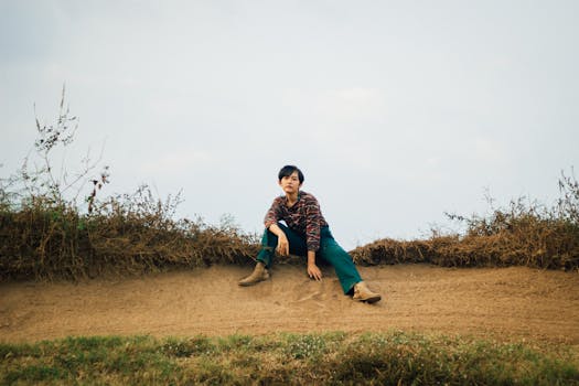 A young woman with short hair posing outdoors on a dirt pathway, surrounded by nature.