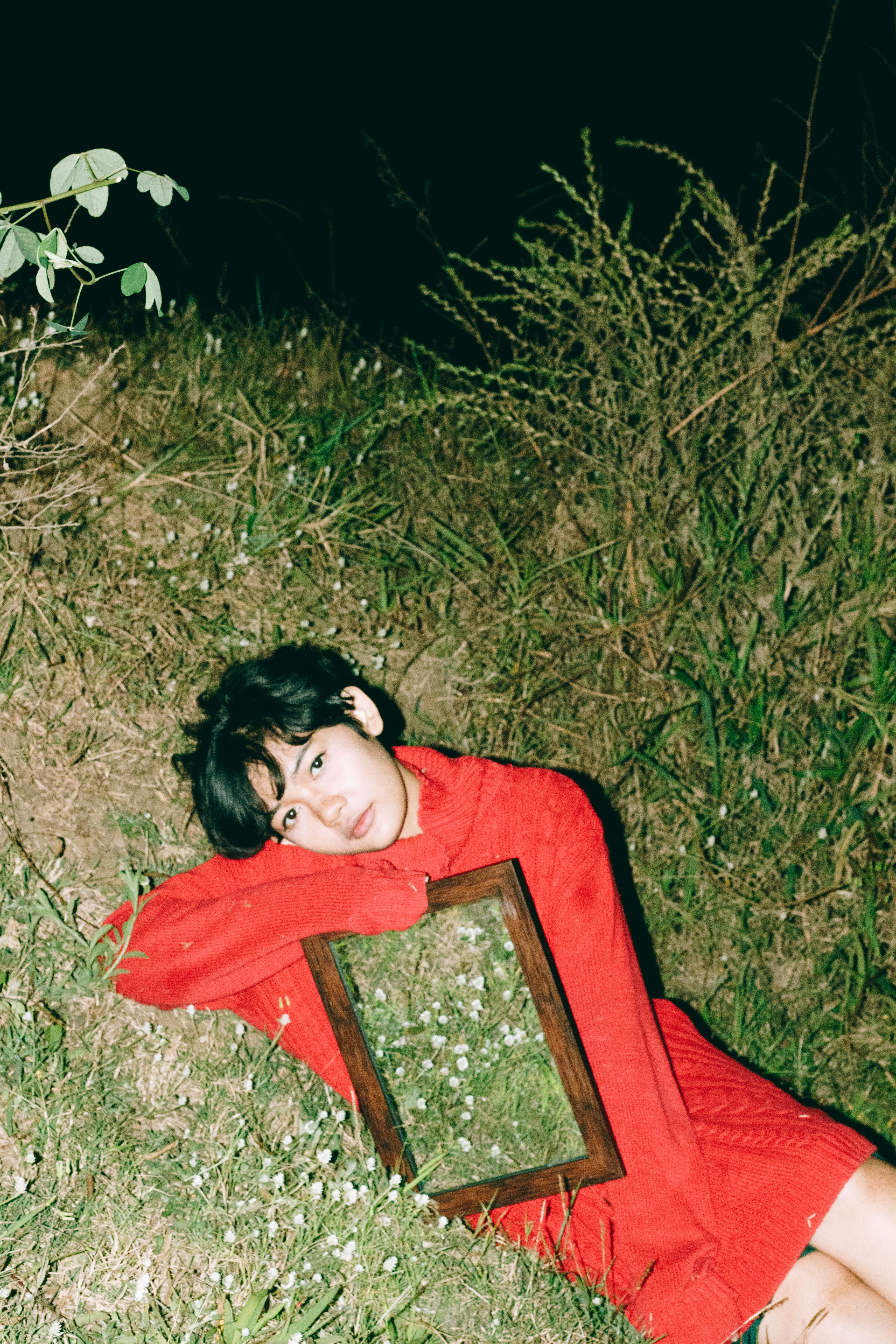 Young woman in red sweater posing with a mirror on grass at night.