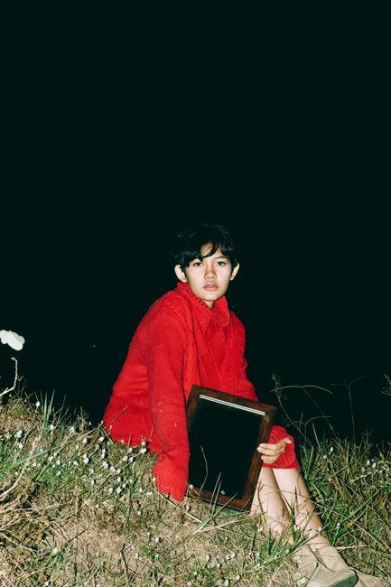 A woman in a red outfit sits outdoors at night holding a frame.