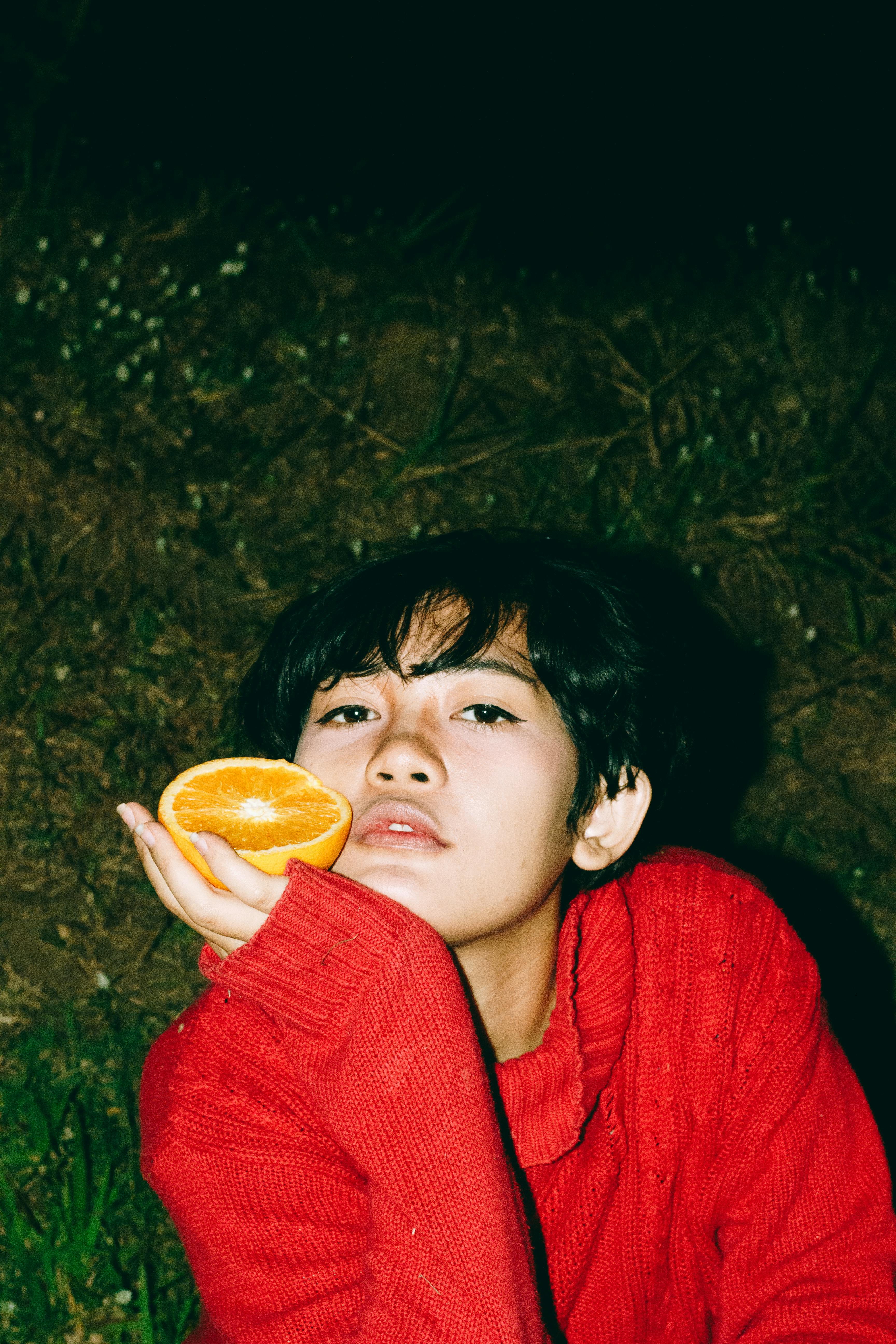Vibrant portrait of a woman in red sweater holding a slice of orange outdoors.
