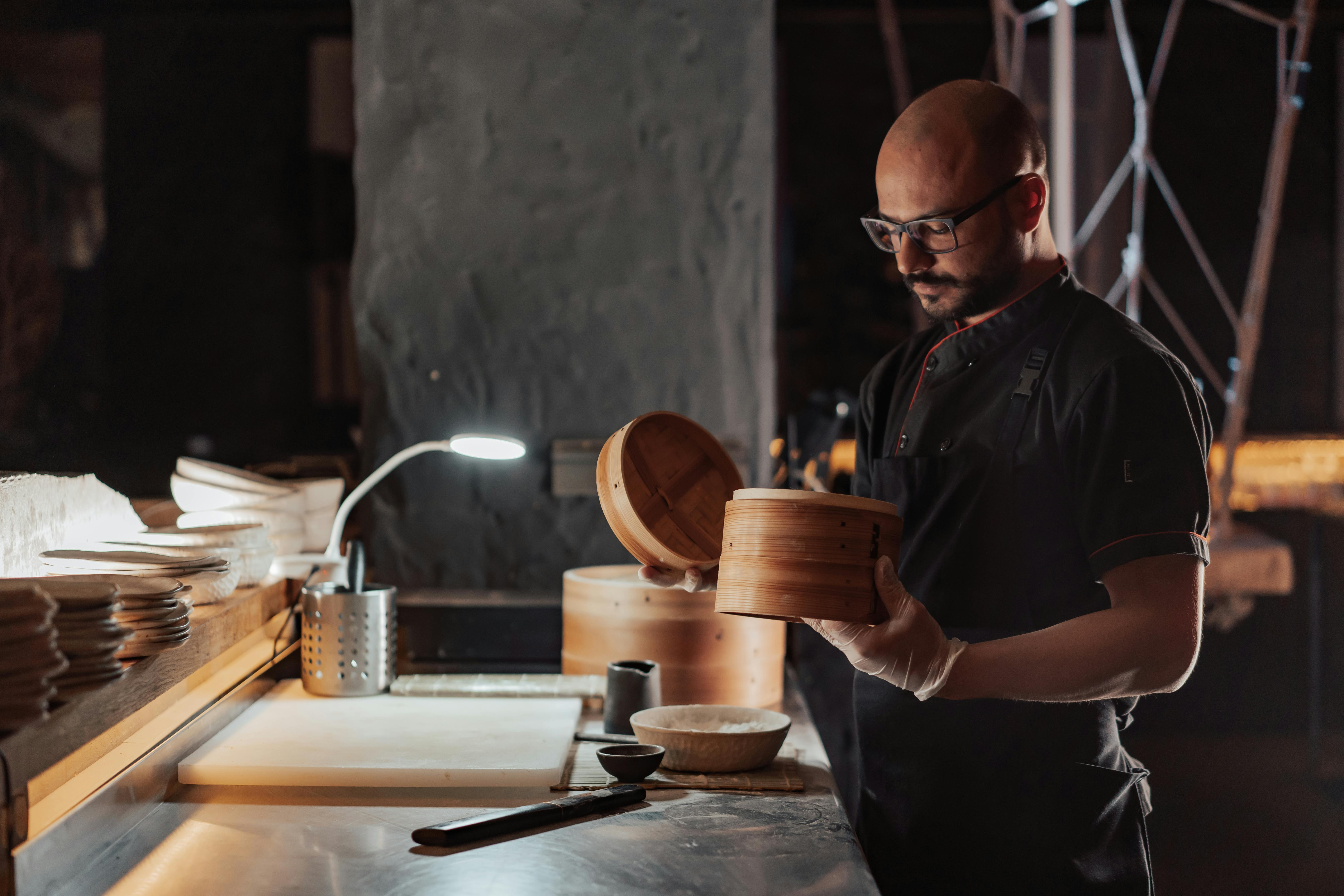 man in black chef uniform holding bamboo steamer basket