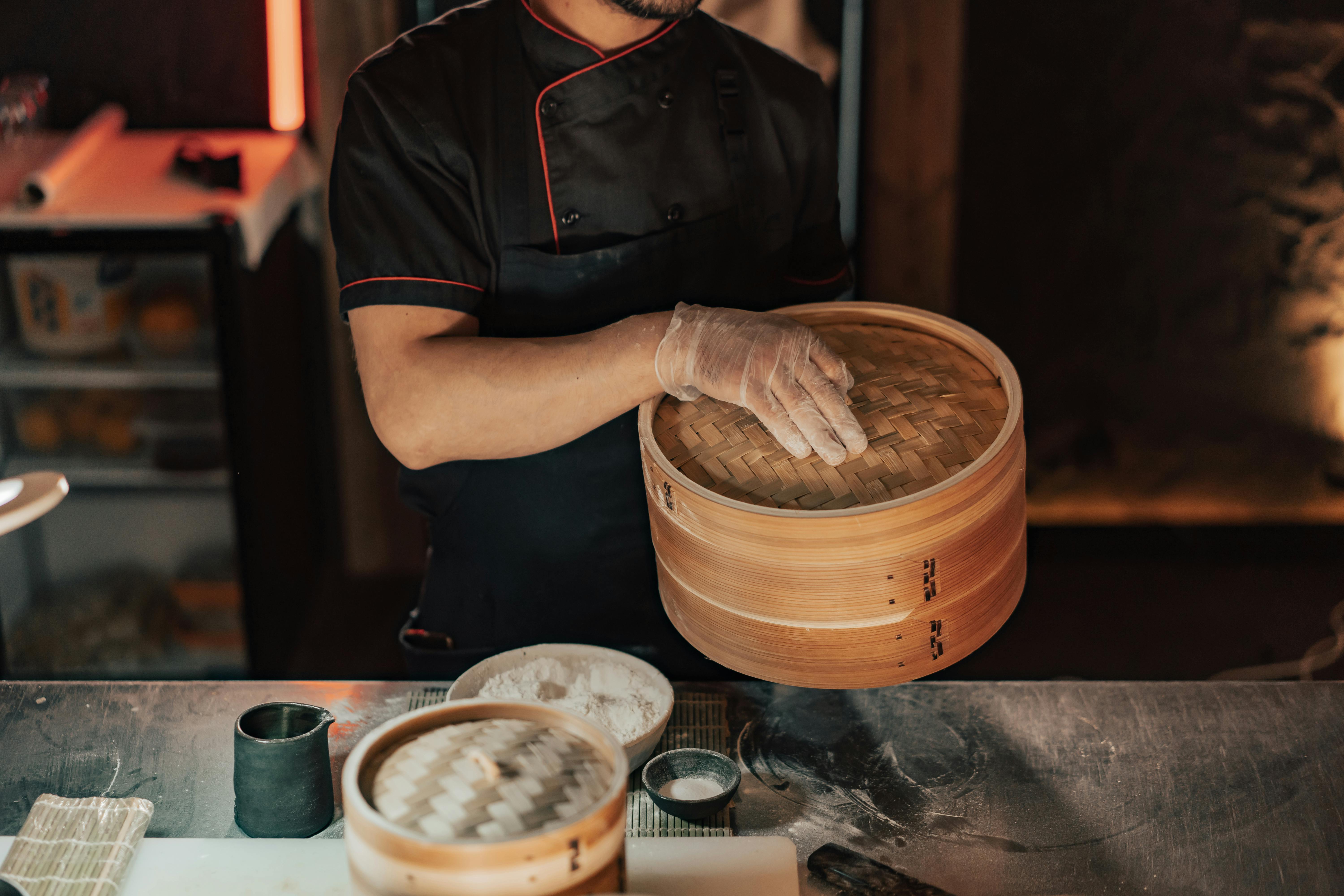 man in black chef shirt holding bamboo steamer basket