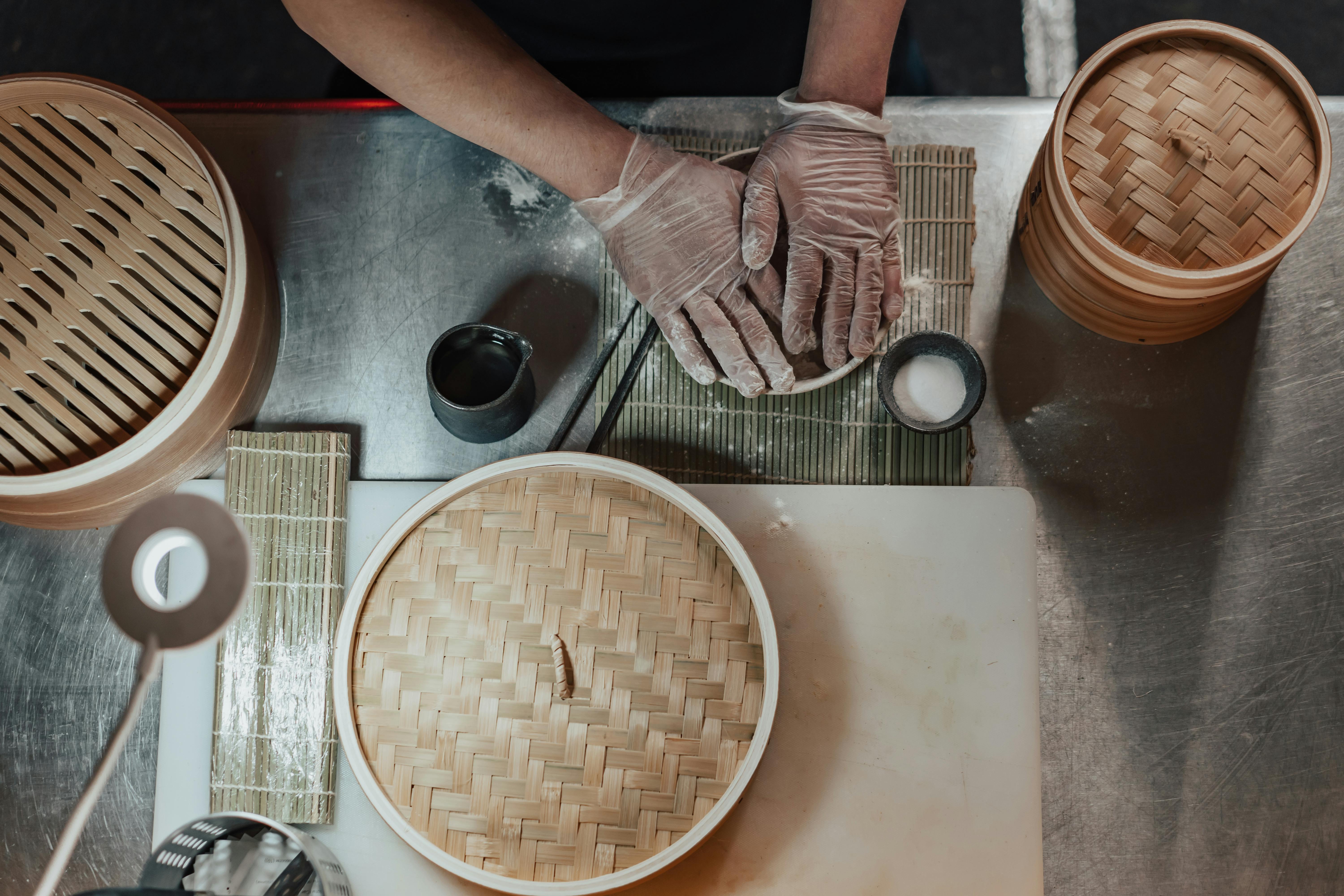 person in gloves cooking on the table beside bamboo baskets