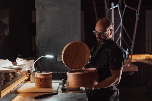 Chef in dark kitchen using bamboo steamer for food preparation, focused and professional.