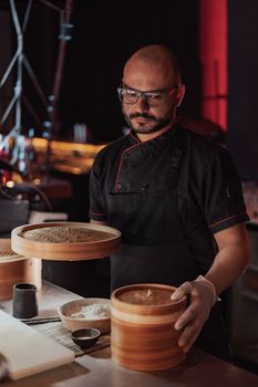 Chef in dark kitchen preparing dim sum using bamboo steamer baskets.