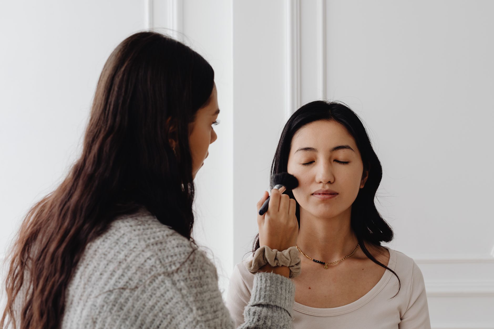 A professional makeup artist applies foundation to a client's face indoors.