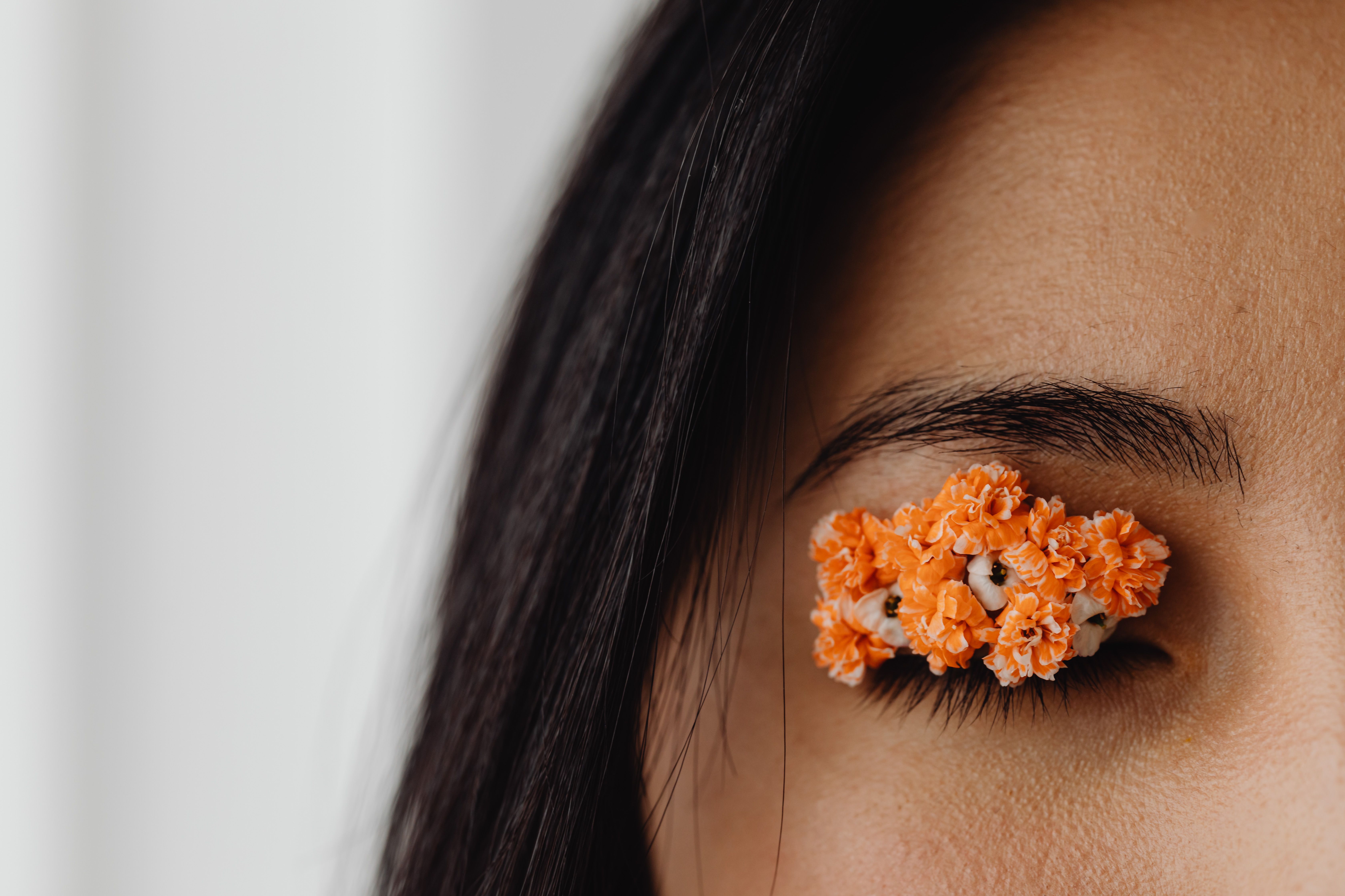 Detailed close-up of a closed eye adorned with intricate orange flower decoration on the eyelid.