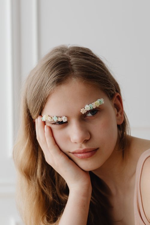 Free Portrait of a young woman with floral decorated eyebrows, resting her face on her hand. Stock Photo