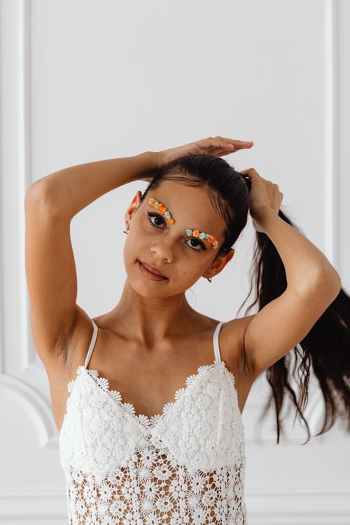 Free Close-up portrait of a woman posing with colorful floral brow art, wearing a white lace top. Stock Photo