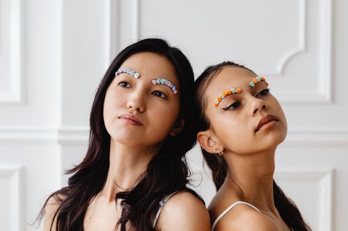 Free Two women posing with creative floral eyebrow decorations in an artistic indoor portrait. Stock Photo