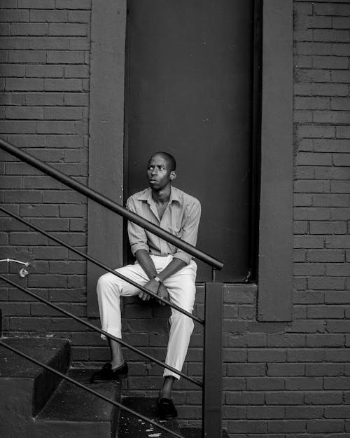 Free Man Sitting on a Ledge of a Brick Wall Near a Stairway Stock Photo