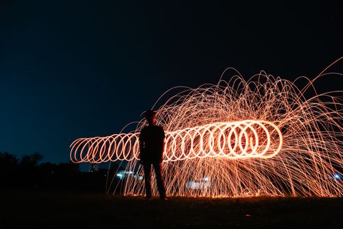 Free Silhouette of anonymous man standing against glowing swing fire during performance on night show Stock Photo