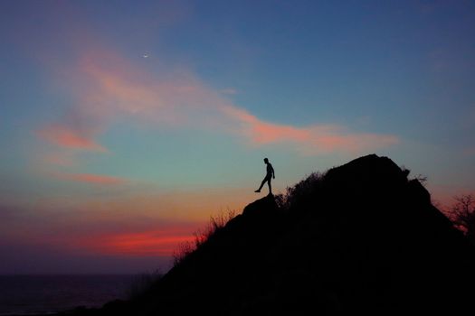 Silhouette of a person standing on a rock at sunset with vibrant sky colors.