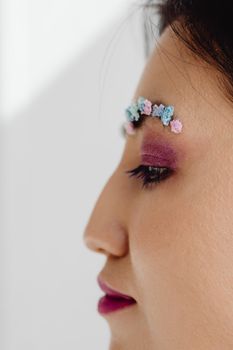 Side profile of a woman with artistic floral eyebrow makeup and pink eyeshadow, emphasizing beauty trends.