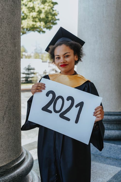 Free Proud graduate holding a '2021' sign in cap and gown. Achievement celebrated outdoors. Stock Photo