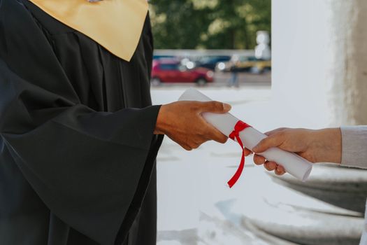 Close-up of a graduate receiving a diploma outdoors in cap and gown.