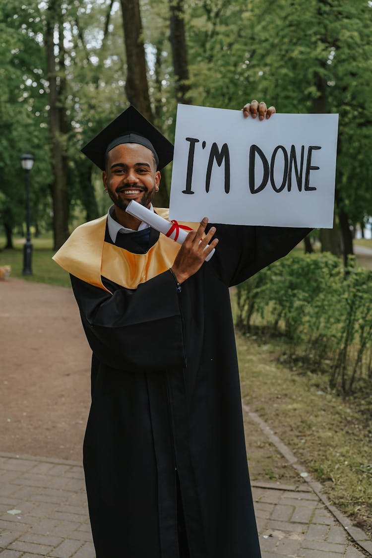 A Man In Black Toga Holding A Signboard And Diploma