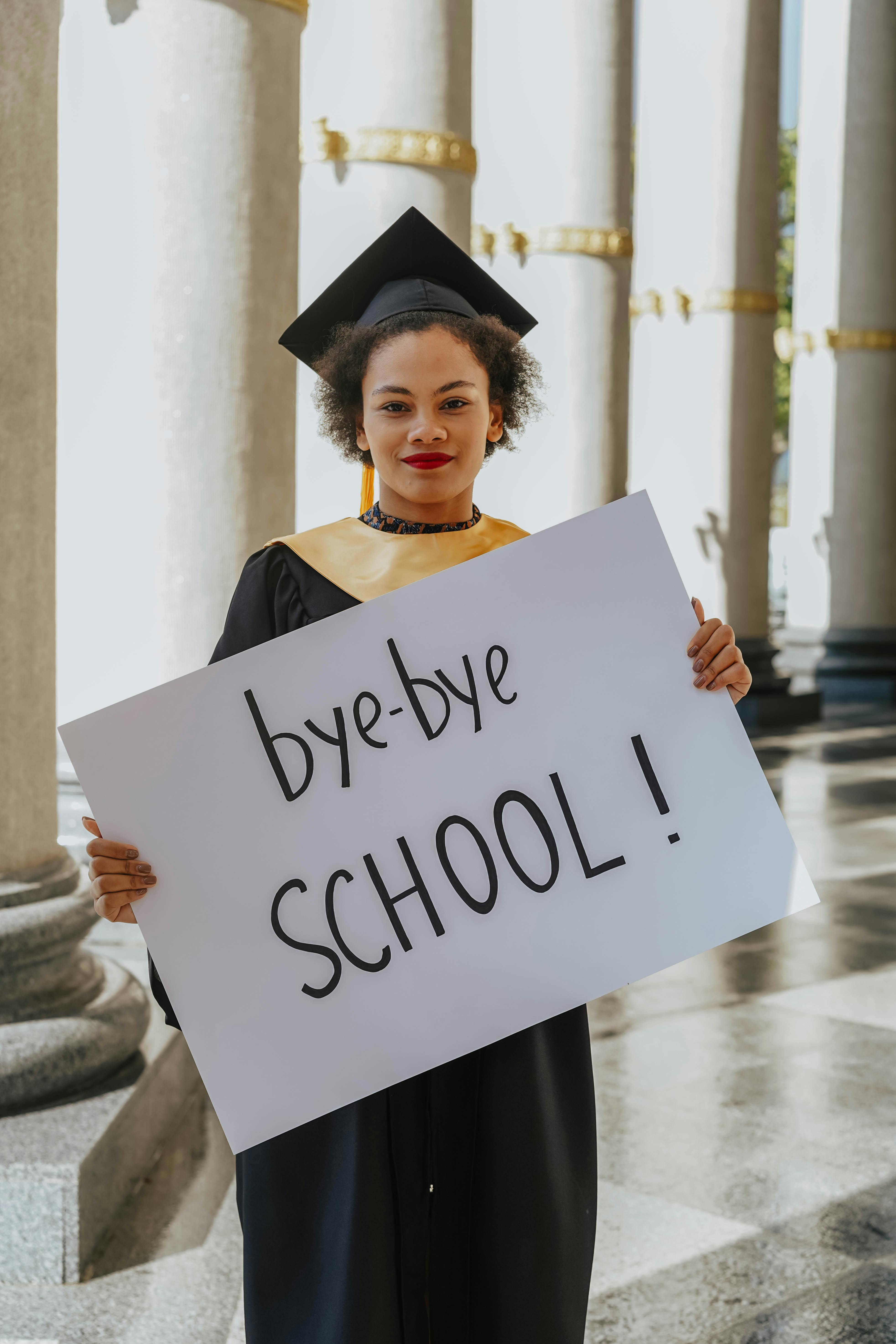 Young woman celebrating graduation holding a 'bye-bye school' sign.