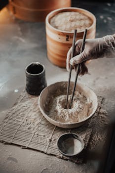 Close-up of hands mixing flour with chopsticks, featuring a bamboo steamer.