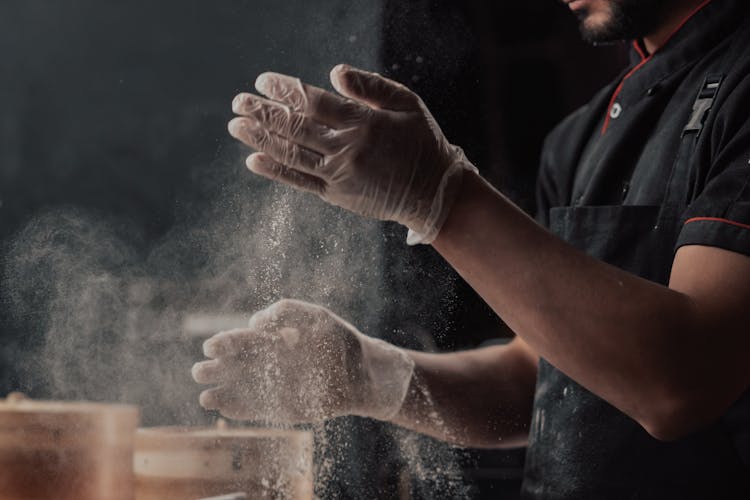 A Man With A Black Apron Shaking Flour From Hands