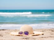 草帽和太阳镜放在沙滩上，背景是蓝色的波浪