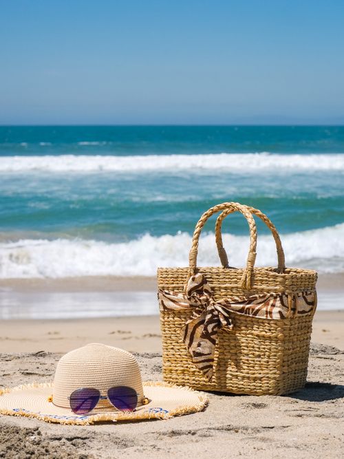 Free A straw hat, bag, and sunglasses laid out on a sunny beach by the ocean. Stock Photo