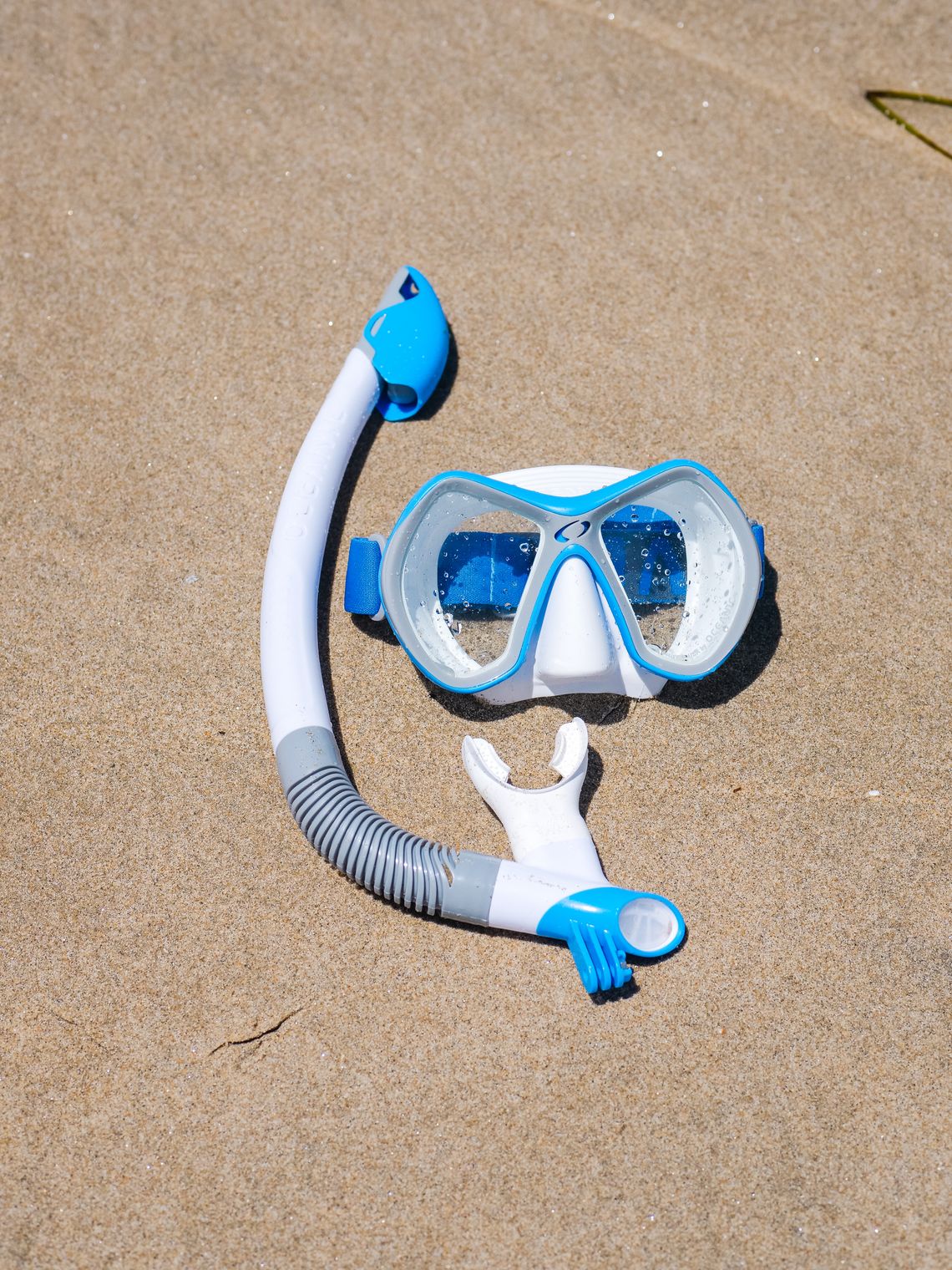 Blue snorkeling mask and snorkel arranged on beach sand