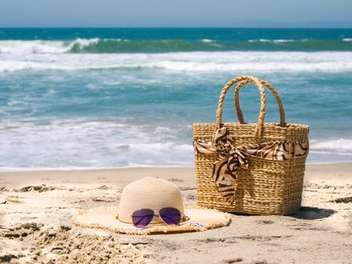 Free Straw hat, beach bag, and sunglasses on sandy beach with ocean waves. Stock Photo