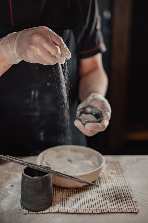 Free Close-up of a chef's hands sprinkling flour over a bowl of dough in a cozy kitchen setting. Stock Photo