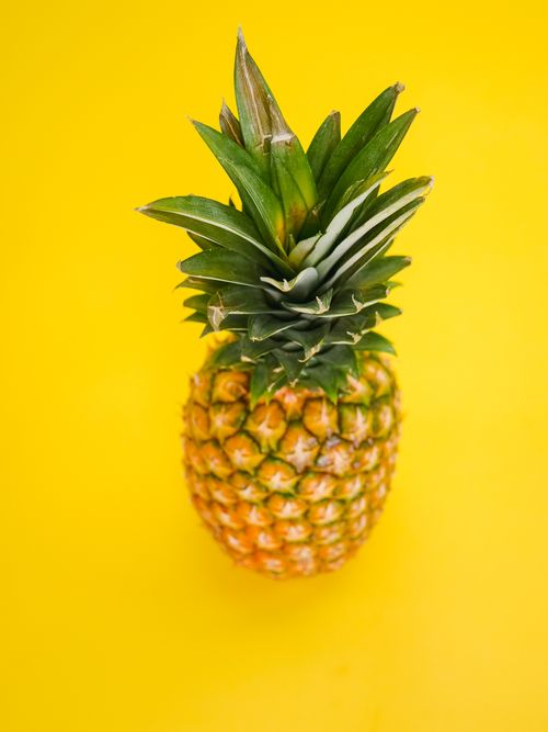 Free Close-up of a ripe pineapple on a vibrant yellow background, showcasing its texture and colors. Stock Photo