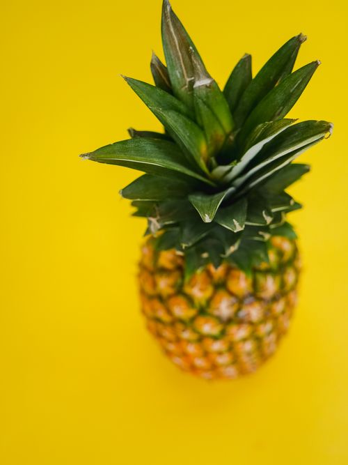 Free Close-up view of a fresh pineapple on a bright yellow background highlighting its tropical vibe. Stock Photo