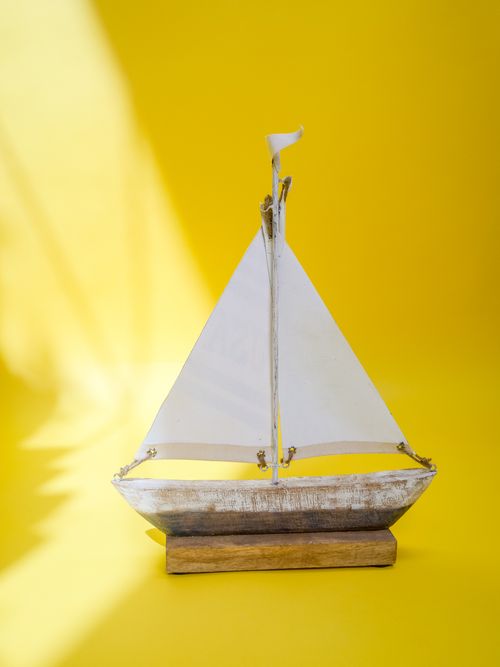 Free A simple wooden sailboat model on a bright yellow background, bathed in sunlight. Stock Photo