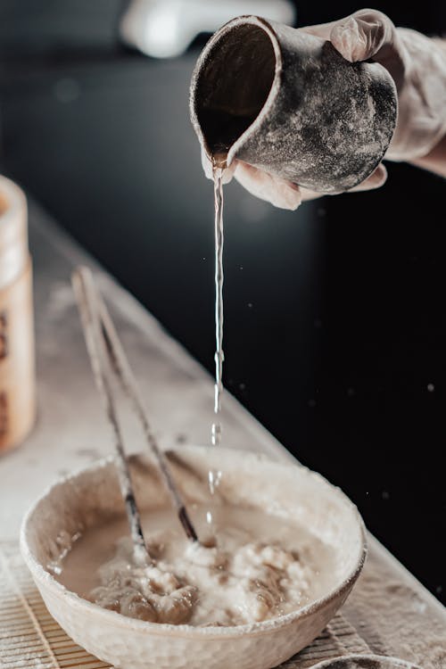 Person Pouring Water on Bowl of Flour