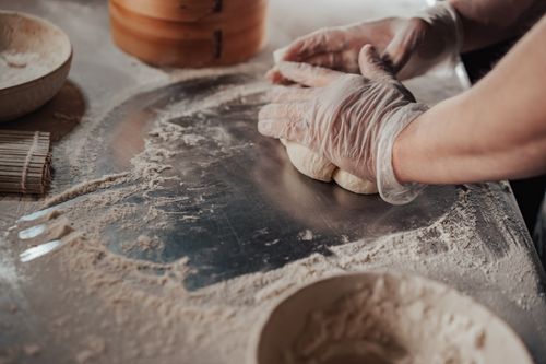Free Hands kneading dough on a floured steel surface with gloves, in a culinary setting. Stock Photo