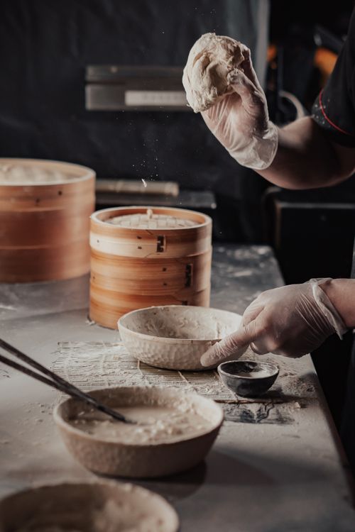 Free Chef skillfully preparing dough with bowls and flour in a rustic kitchen setting. Stock Photo