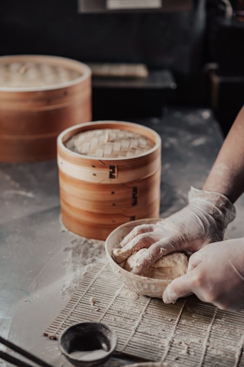 Free Close-up of hands kneading dough for dim sum over mat with steamer baskets nearby. Stock Photo